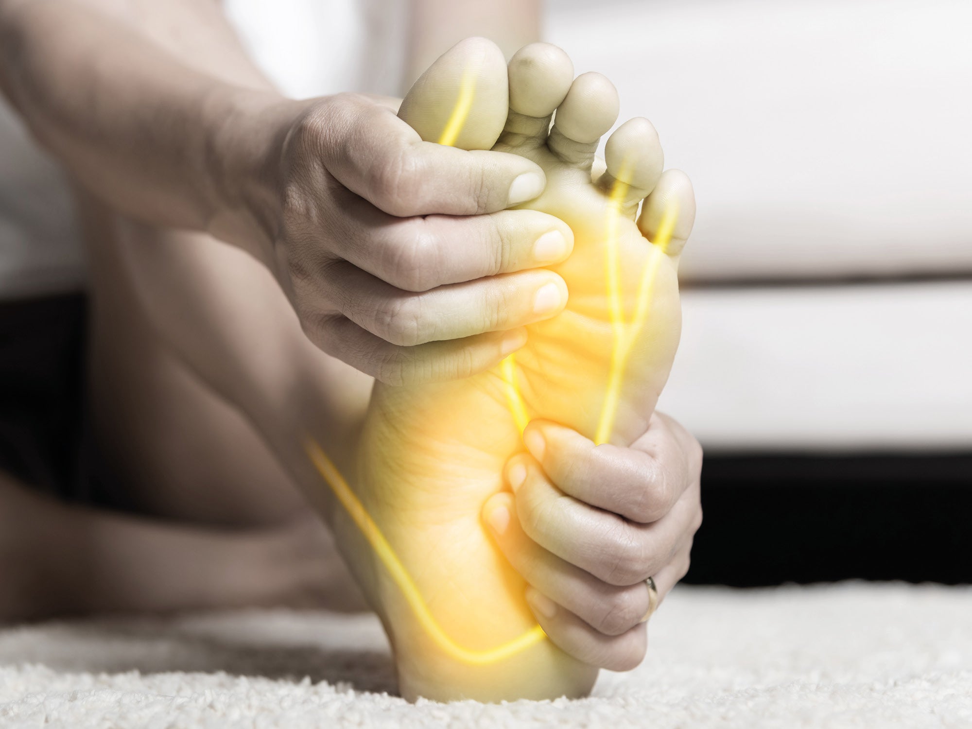 Gros plan d'un pied tenu par des mains. Des lignes jaunes sur la plante du pied symbolisent la douleur nerveuse ou l'inconfort dans les terminaisons nerveuses.